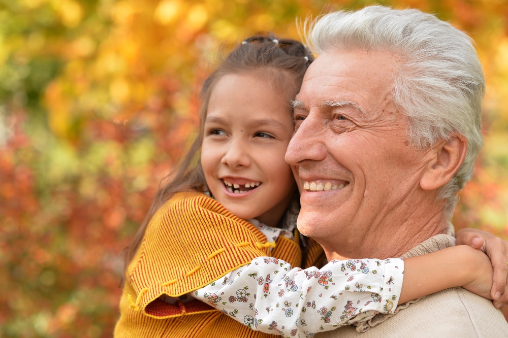 senior man with smiling granddaughter outside in fall