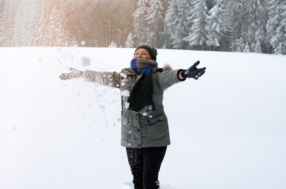 Senior woman in winter clothing throwing snow outside